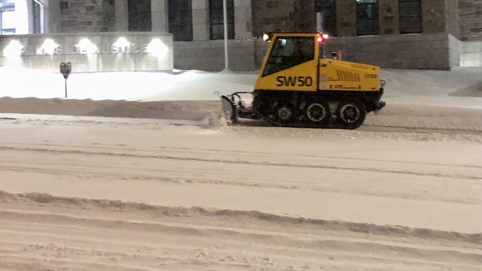 Un petit tracteur à chenilles déneige un trottoir.