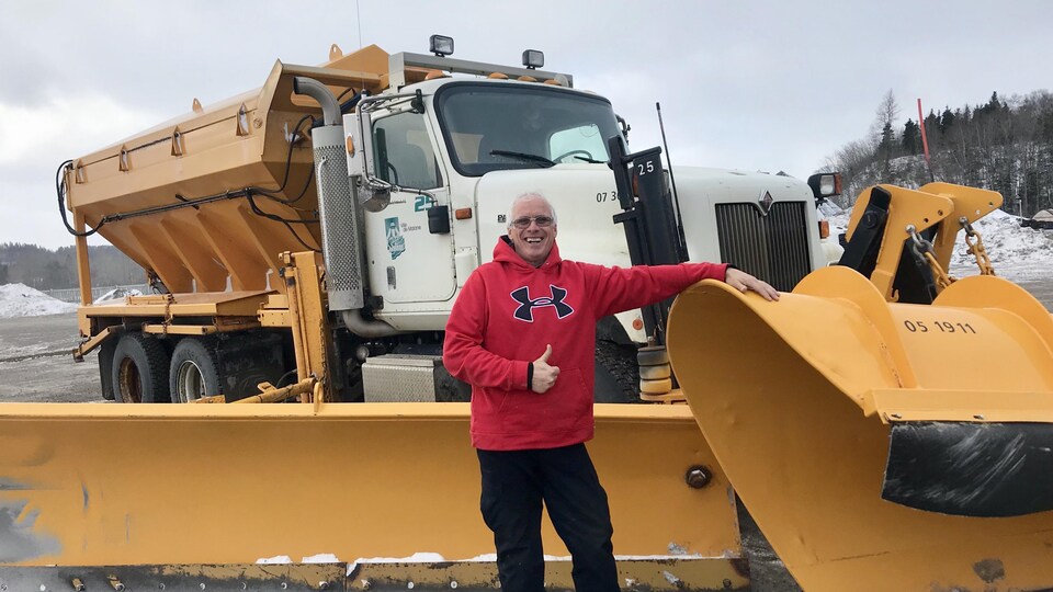 Un homme prend la pose devant un camion de déneigement.