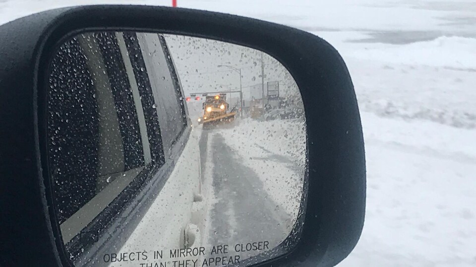 Un véhicule de déneigement vue à partir du rétroviseur d'une voiture