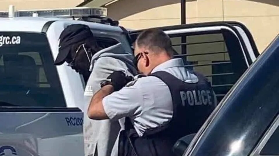 Un policier tient l'accusé menotté dans le dos, quelques instants avant de l'asseoir dans une camionnette de la GRC.