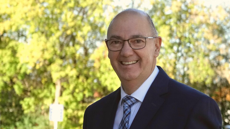 Denis Tassé souriant, portant complet et cravate