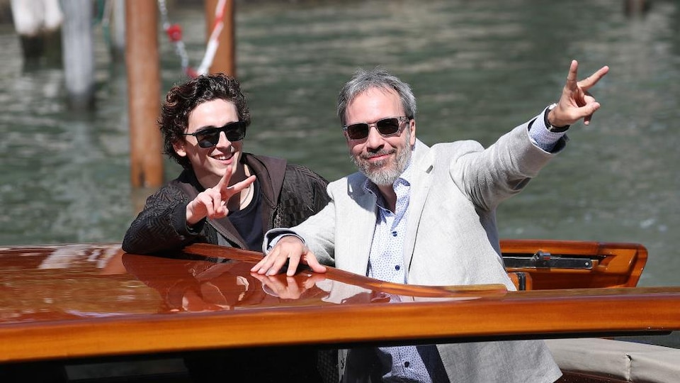 Deux hommes sont sur un bateau et saluent la foule.