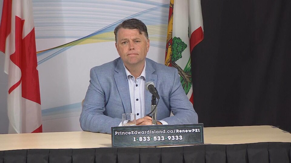Dennis King, assis à une table devant un drapeau du Canada et un drapeau de l'Île-du-Prince-Édouard.