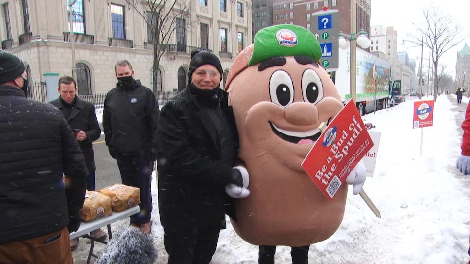 Sous la neige, le premier ministre King tient par la main une mascotte en forme de grosse patate.