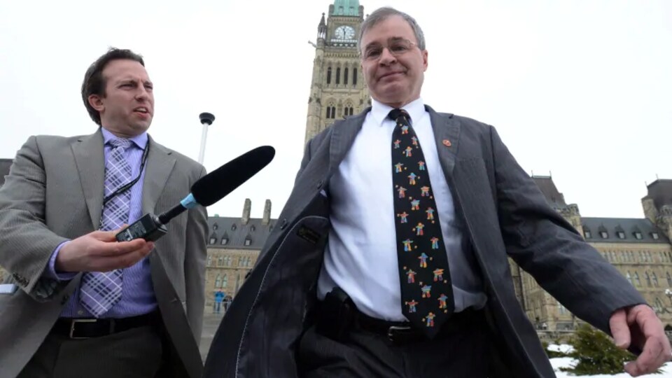 Un reporter tend un micro vers Dennis Patterson qui marche devant le Parlement à Ottawa.