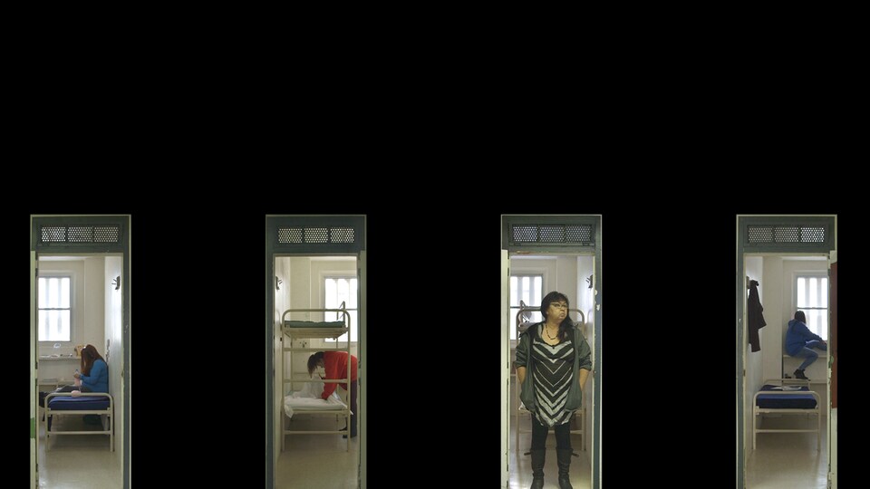 Quatre vidéos verticales projetées sur un mur noir montrent des femmes dans leurs cellules de prison. 