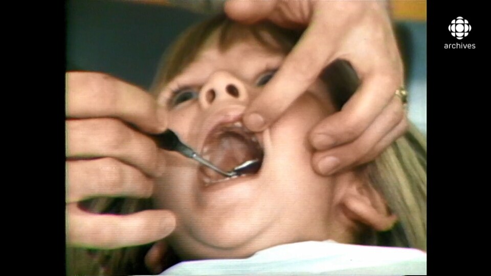 Une enfant d'âge préscolaire, la bouche grande ouverte, dont les dents sont examinées avec un instrument de dentiste.