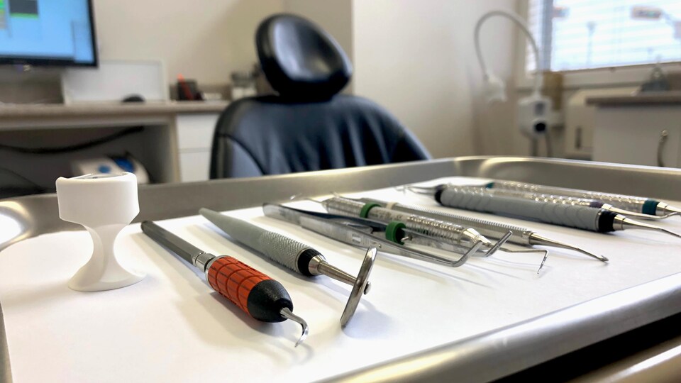 Outils de dentiste sur une table avec une chaise en arrière plan.