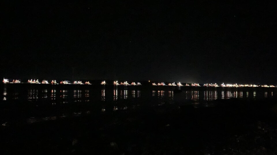 Une ligne de lumières de bateaux perce la noirceur du petit matin.
