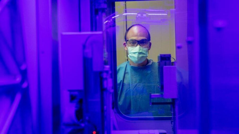 Un homme vêtu d'un sarrau, le visage couvert d'un masque et portant des lunettes de protection est photographié dans un laboratoire de microbiologie.