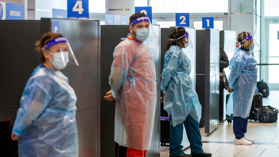 Quatre travailleurs de la santé portant de l'équipe de protection sont debout devant leurs cubicules à l'aéroport.