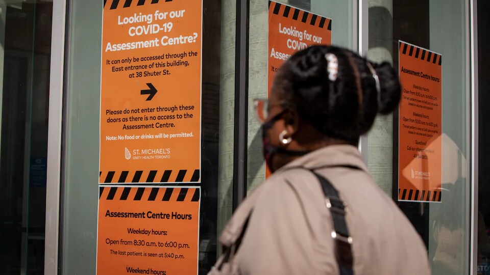 Une femme regarde les enseignes sur le dépistage de la COVID-19 à l'entrée d'un hôpital de Toronto.