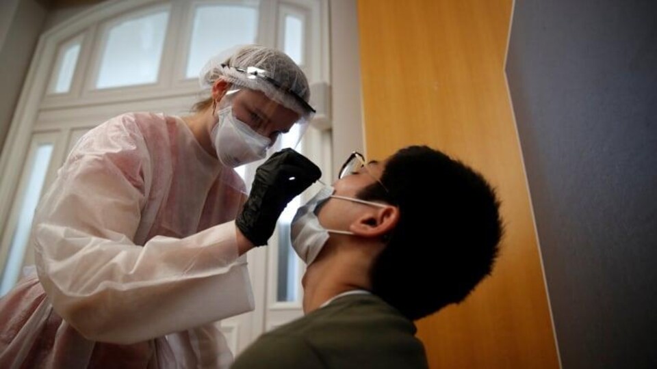 Une infirmière en combinaison de sécurité avec masque et charlotte et gants fait un test de dépistage à la covid-19 à un homme.