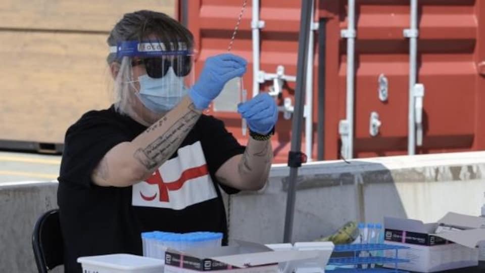 Une personne qui porte un t-shirt sur lequel on voit un drapeau mi'kmaw fait l'analyse des échantillons à un site extérieur de dépistage de COVID-19.