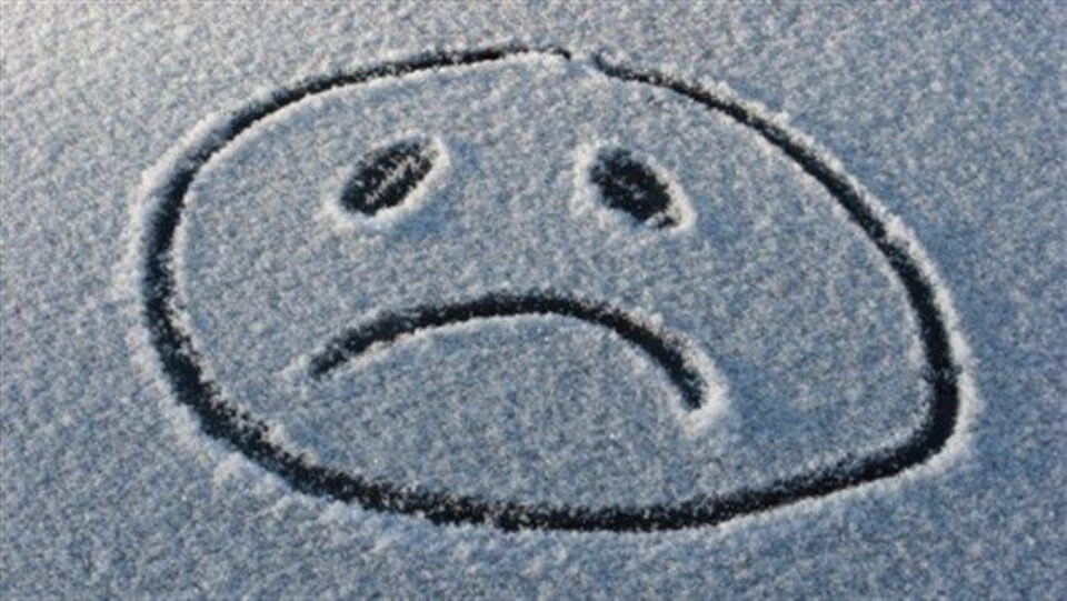 Le blues de l'hiver représenté par le dessin d'un visage triste dessiné dans la neige. 