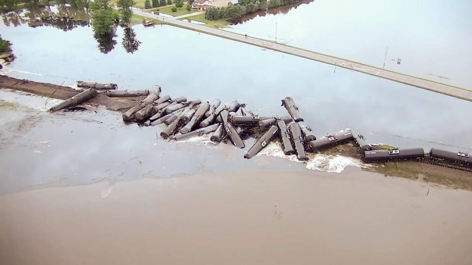 Vue aérienne d'une trentaine de wagons-citernes qui sont empilés sur une voie ferrée inondée.