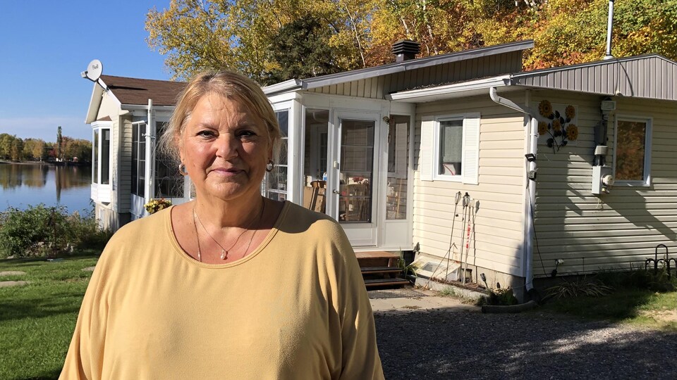 Une femme pose devant son chalet sur le bord d'un lac l'automne.