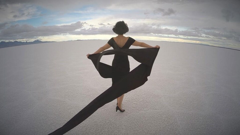 Vêtue d'une robe à volants et chaussée d'escarpins noirs, une femme marche dans le désert.
