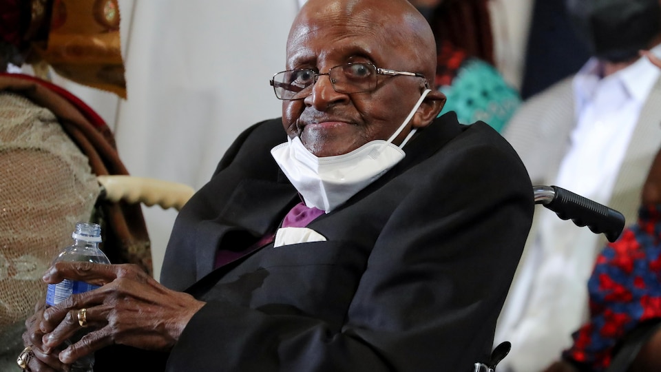 Assis dans un fauteuil roulant, Desmond Tutu regarde vers la caméra. 