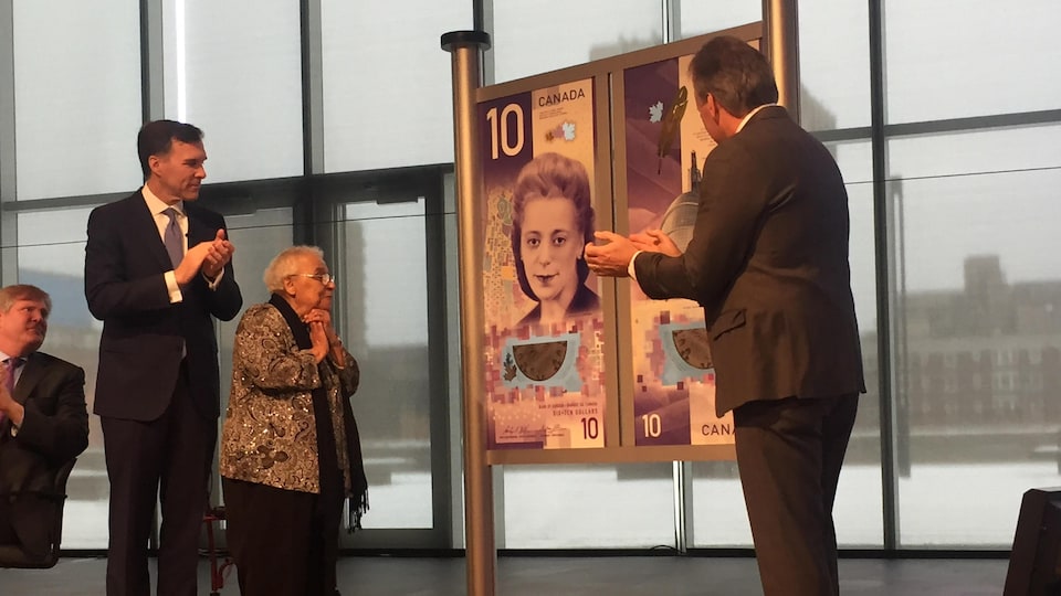 Les dignitaires entourent une grande affiche illustrant le nouveau billet de banque de 10 $.