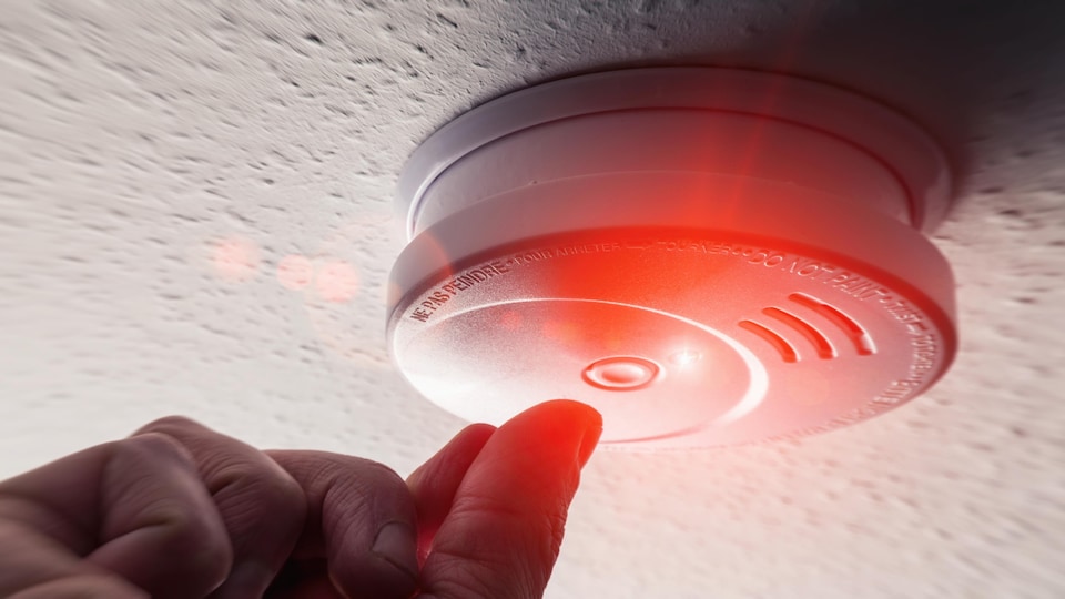La lumière rouge d'un détecteur de fumée installé au plafond est allumée.