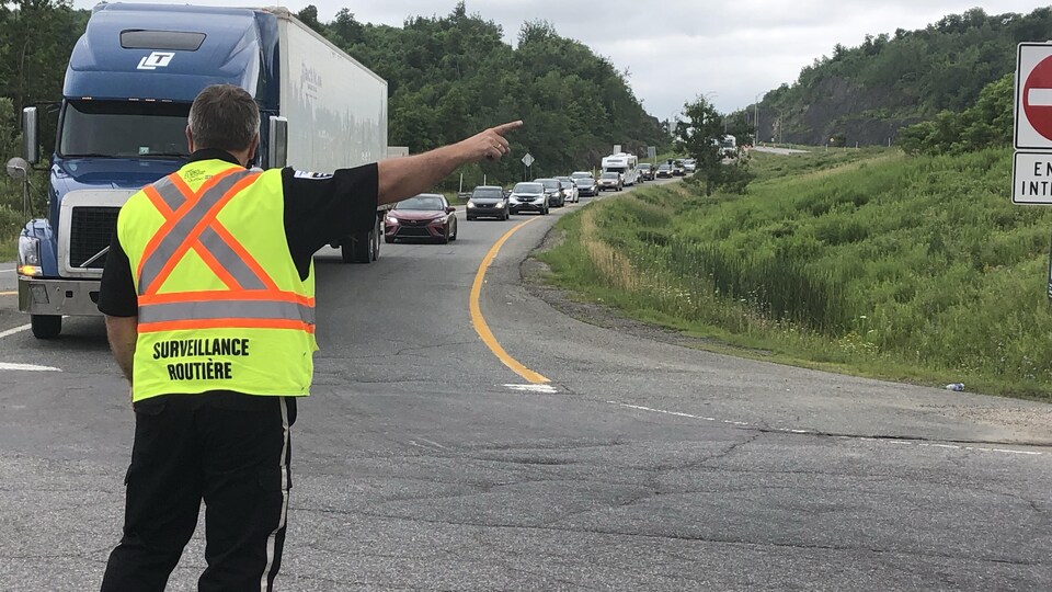 Un homme redirige une longue file de véhicules arrêtés sur l'autoroute. 