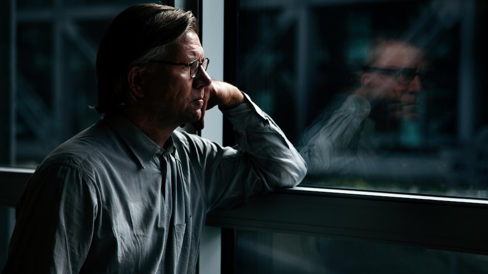 Un homme pensif regarde par la fenêtre de son bureau.