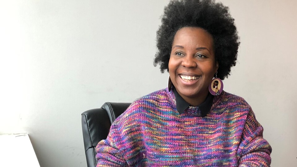 Une femme noire assise et souriante en pull coloré