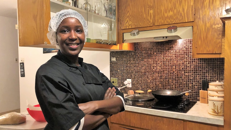 Une femme en tablier noir et cheveux couverts d'un filet blanc dans sa cuisine