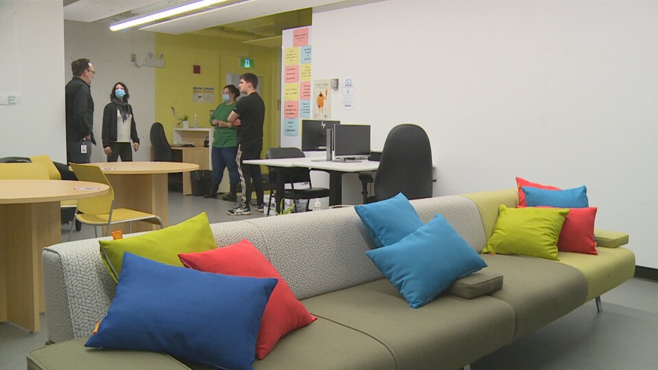 Un sofa avec des coussins multicolores près duquel un groupe de gens discutent.