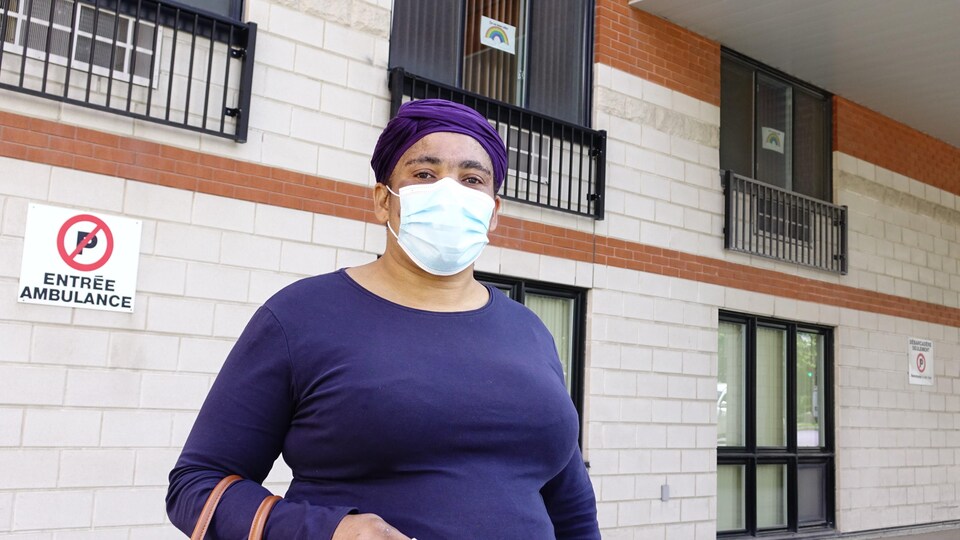 Guerline Calixte porte un masque et se tient debout devant le mur d'une résidence.