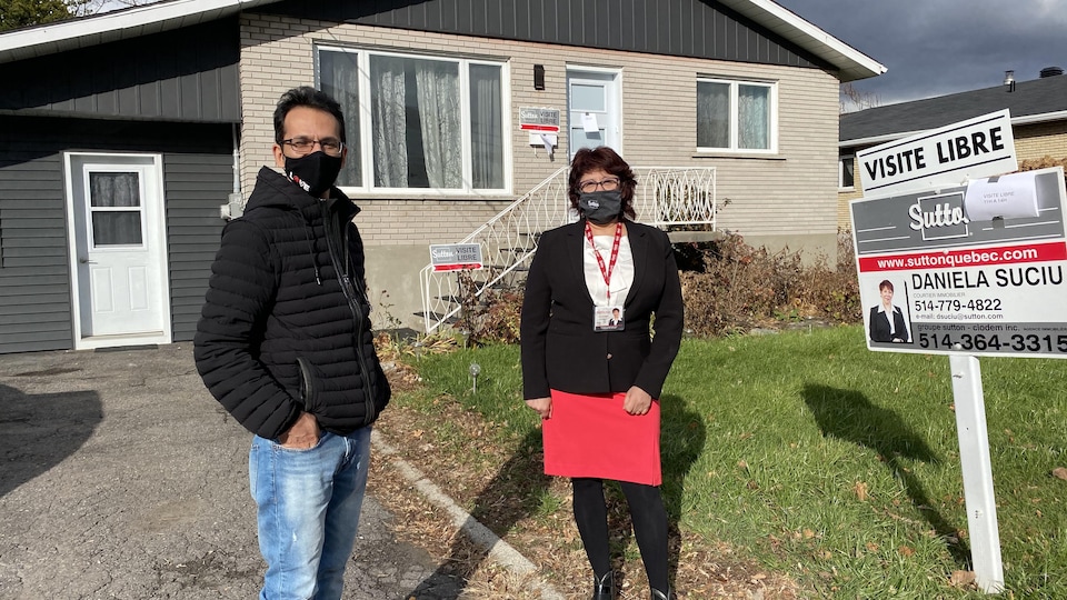 Alic et Daniela portant un masque posant devant une maison à vendre