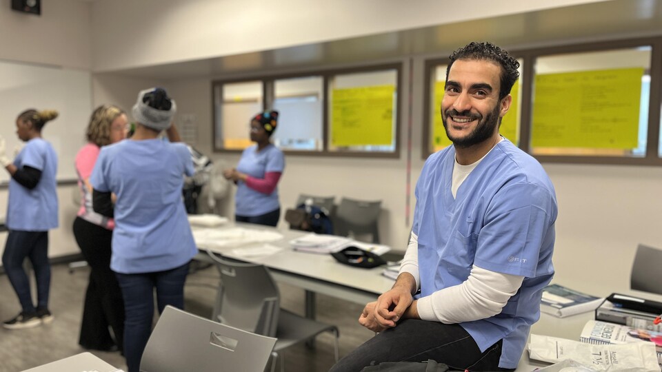 Hicham, souriant, assis sur une table de la salle de classe. 