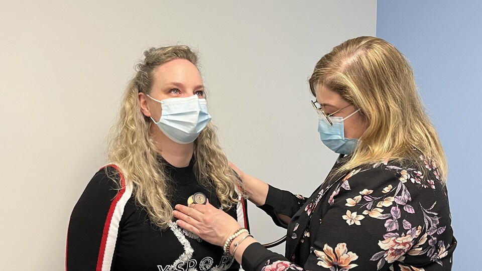 A nurse examines a woman with curly blonde hair.