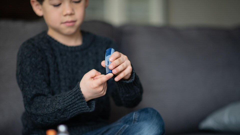 Un enfant assis se pique le doigt pour obtenir une goutte de sang.