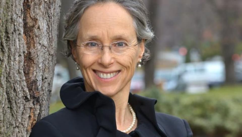 Une femme souriante est adossée à un arbre