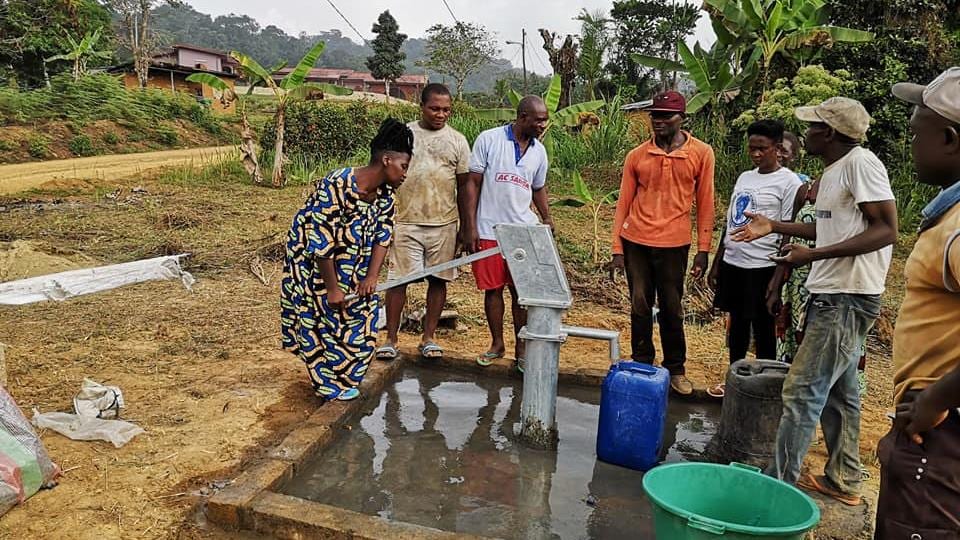 Un groupe de personnes autour d'une fontaine à eau qui fonctionne avec une pompe à actionner.
