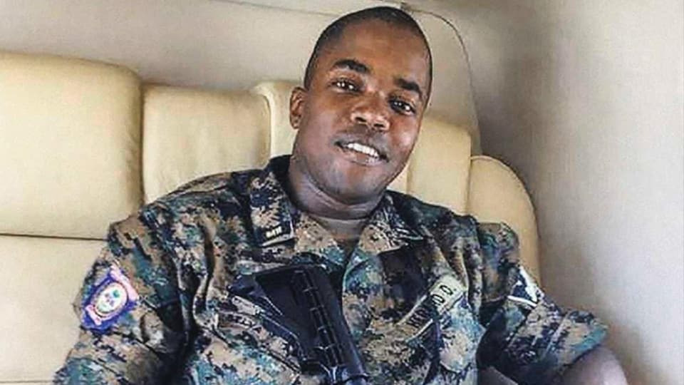 Dimitri Hérard, assis, portant un uniforme militaire et un fusil.