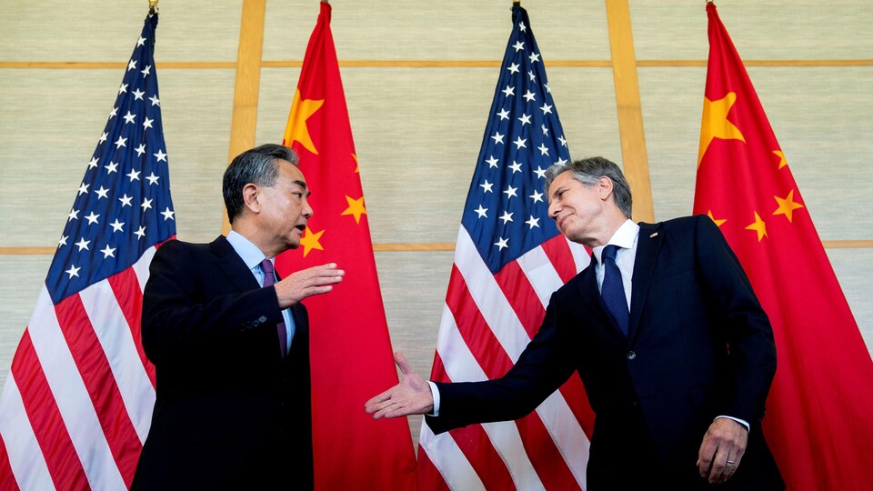 Anthony Blinken se penche pour serrer la main à Wang Yi devant des drapeaux américains et chinois. 