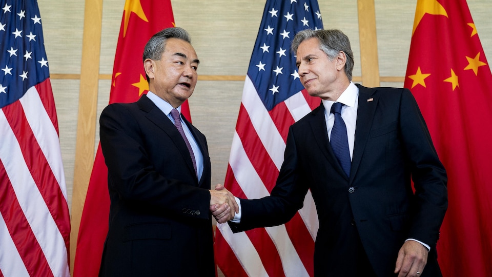 Wang Ye ve Anthony Blinken bayrakların önünde el sıkışıyor.