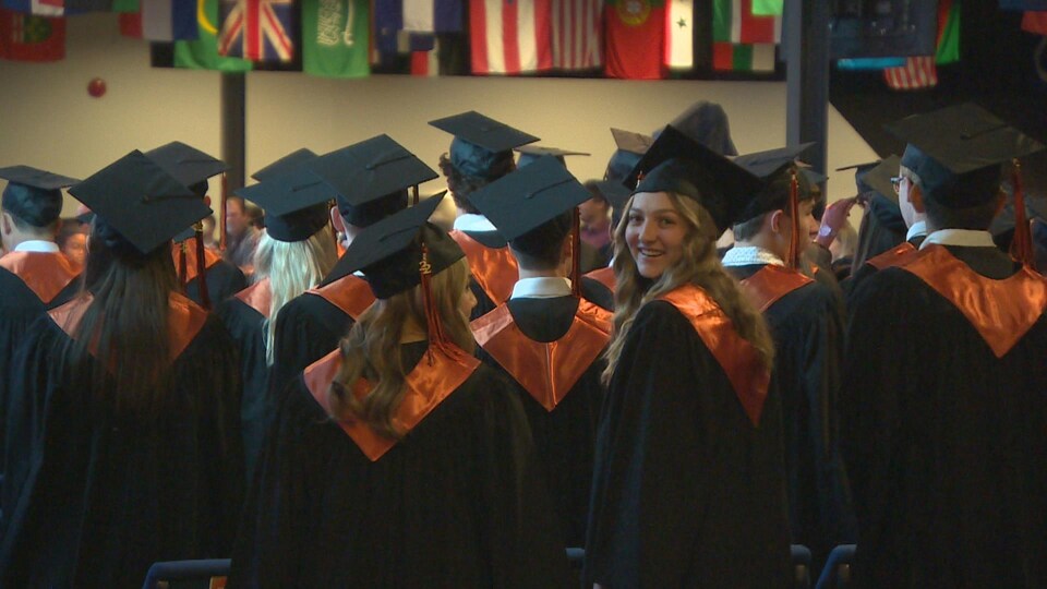 Photo des élèves diplômés de dos avec leurs uniformes noirs et oranges. 