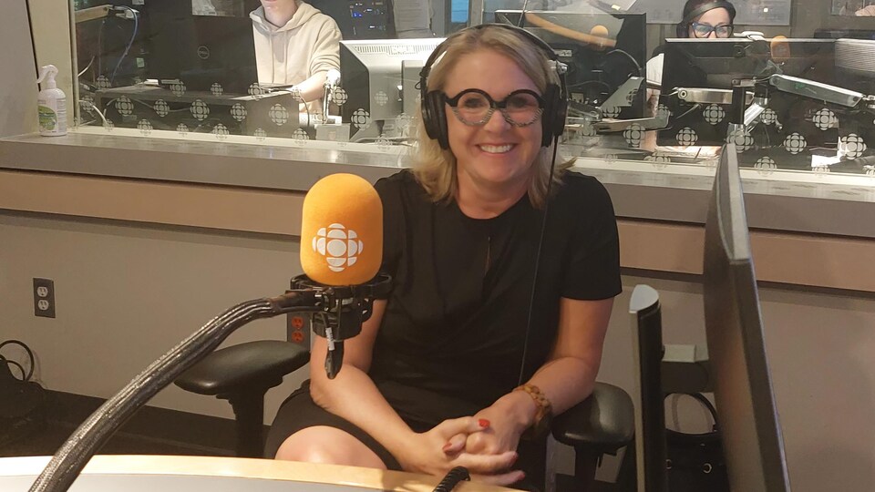 Une femme, derrière le micro de Radio-Canada, sourit à la caméra. 