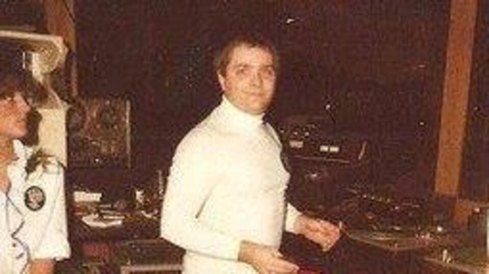 Dressed in white, Robert Ouimet poses in the booth where he mixes the music.