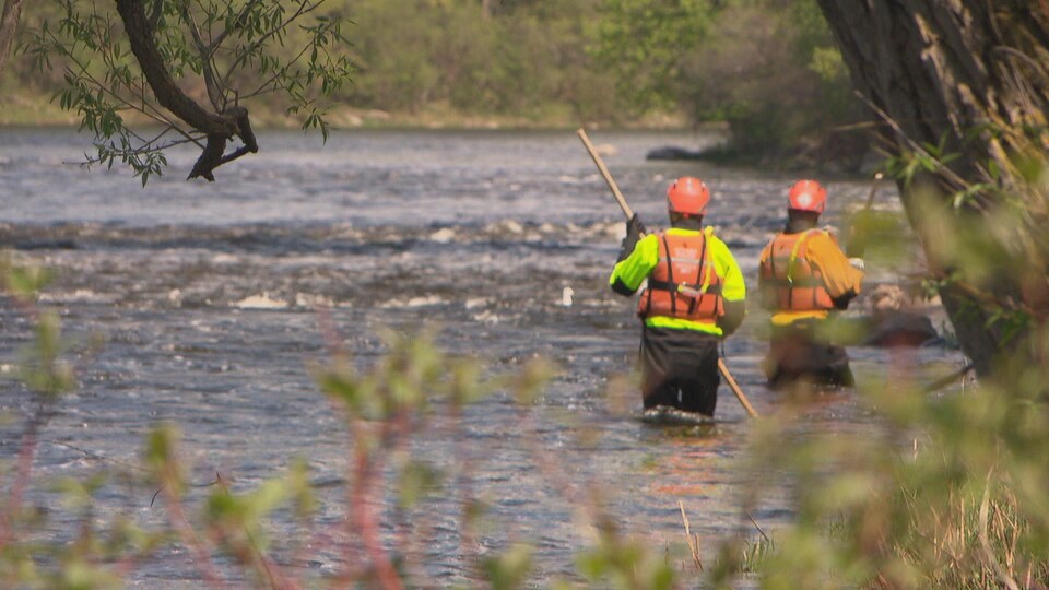 Deux agents munis de vestes de flottaison effectuent des recherches dans l'eau.