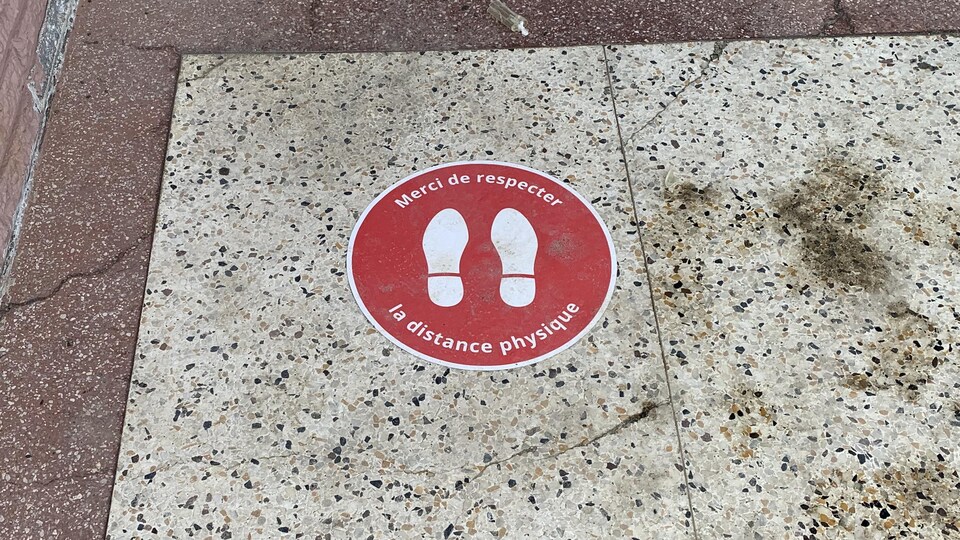 Un collant par terre indique « merci de respecter la distance physique ».