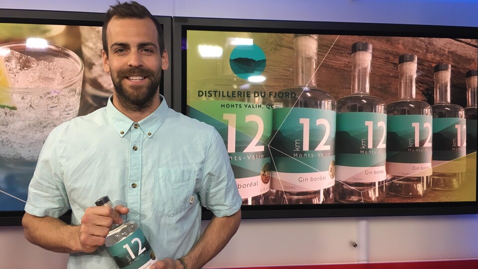 Un homme barbu tient dans ses mains une bouteille de gin KM12.