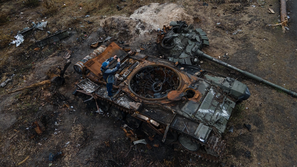 A man takes a picture of a destroyed Russian army tank.