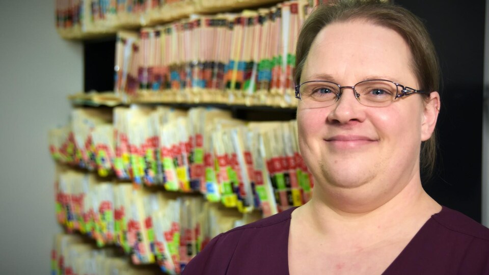 Femme souriante devant des étagères de dossiers médicaux.