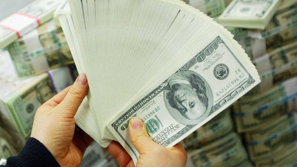Deux mains tiennent des dizaines de billets de banque américains.