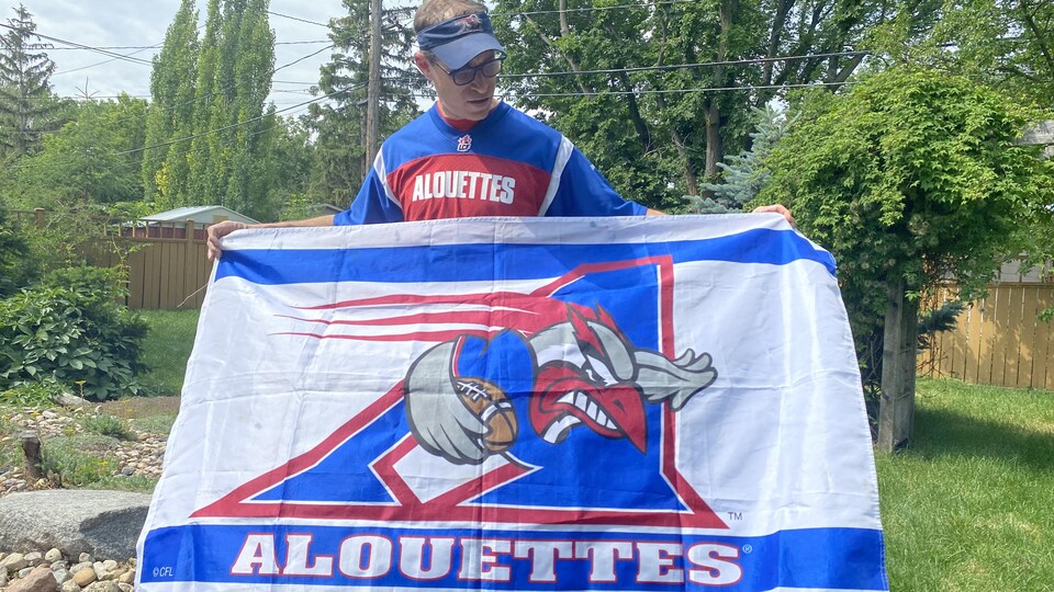Dominic Blais, amateur de football, tient un drapeau des Alouettes de Montréal dans sa cour arrière à Regina le 2 juillet 2022